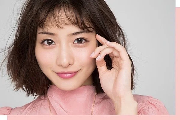 Hình ảnh cute nữ với cô gái trẻ tóc bob nâu, mặc áo hồng pastel và mỉm cười nhẹ trước phông nền studio