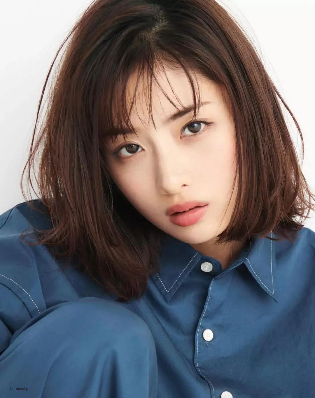 Hình ảnh cute nữ với cô gái tóc nâu ngang vai mặc áo xanh denim, tạo dáng cận cảnh trên nền trắng
